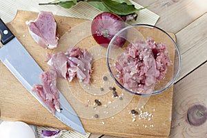 Raw chopped pork tenderloin with herbs in a glass bowl on a wooden board