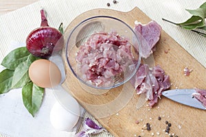 Raw chopped pork tenderloin with herbs in a glass bowl on a wooden board