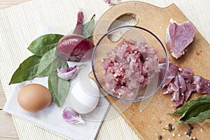 Raw chopped pork tenderloin with herbs in a glass bowl on a wooden board