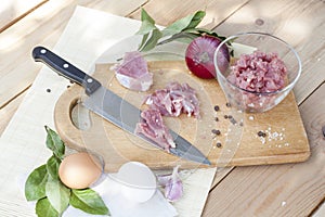 Raw chopped pork tenderloin with herbs in a glass bowl on a wooden board