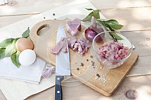 Raw chopped pork tenderloin with herbs in a glass bowl on a wooden board