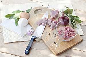 Raw chopped pork tenderloin with herbs in a glass bowl on a wooden board