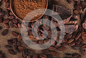 Raw cocoa beans, clay bowl with cocoa powder, chocolate on sack