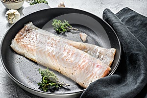 Raw cod fillet with thyme and herbs in a pan. Cooking fresh fish. Gray background. Top view