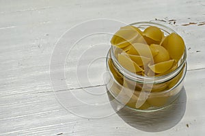 Raw Conchiglie Pasta in glass jar on white wooden background