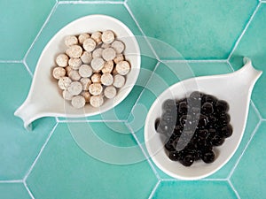 Raw and cooked tapioca balls with different flavors, also known as boba in bubble tea, on green tile background.