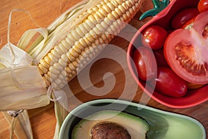 A raw corn  and two bowls that are adapted for tomatoes and avocados