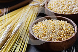 Raw couscous in bowl on wooden background with wheats