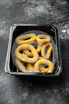 Raw crispy squid rings in breadcrumbs package, on black dark stone table background