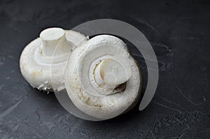 Raw cultivated champignon mushrooms on dark grey slate background. Vegitarian food cooking