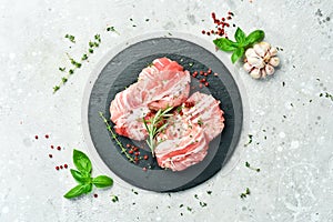 Raw cutlets in bacon served on a black plate with rosemary and thyme. On a gray background.