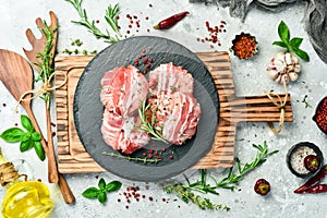 Raw cutlets in bacon served on a black plate with rosemary and thyme. On a gray background.