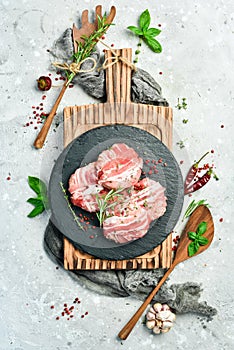 Raw cutlets in bacon served on a black plate with rosemary and thyme. On a gray background.