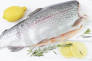 A raw decapitated trout sliced on one side with a lemon and rosemary leaves next to it. Freshwater fish