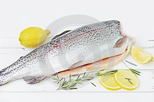 A raw decapitated trout on a white background sliced on one side with a lemon and rosemary leaves next to it. Freshwater fish