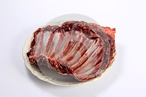 Raw deer ribs on a white plate, white background. Meat of wild animals