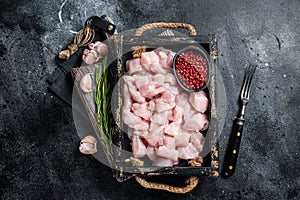 Raw Diced chicken breast fillets, sliced poultry meat in wooden tray. Black background. Top view
