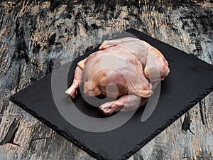 Raw domestic chicken carcass on a black slate board