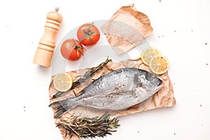 Raw dorada fish or gilt-head bream on ice with lemon, tomato, rosemary and salt over white background, flat lay, top