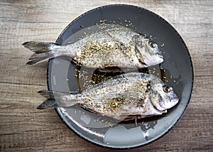 Raw dorado fish on a plate sprinkled with spices before cooking by the chef