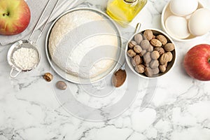 Raw dough, nutmeg seeds and other ingredients on white marble table, flat lay. Space for text