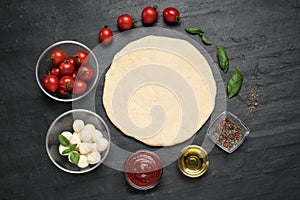 Raw dough and other ingredients for pizza on black table, flat lay