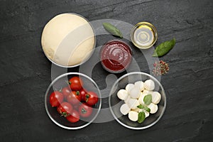 Raw dough and other ingredients for pizza on black table, flat lay