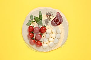 Raw dough and other ingredients for pizza on yellow background, top view