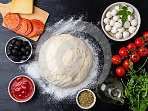 Raw dough for pizza with ingredients and spices on dark black ba