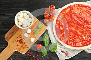 Raw dough for pizza with red sauce and ingredients on table, top view