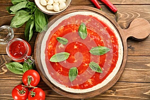 Raw dough for pizza with red sauce and ingredients on table, top view