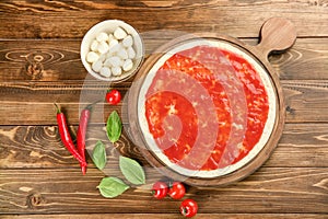 Raw dough for pizza with red sauce and ingredients on table, top view