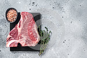 Raw dry aged wagyu porterhouse beef steak, uncooked T-bone on marble board with thyme. Gray background. Top view. Copy