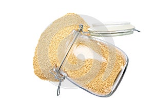 Raw dry amaranth spill out of a glass storage jar isolated on white background top view
