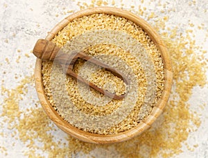 Raw Dry bulgur wheat grain in a wooden bowl with a scoop top view. Mediterranean cuisine