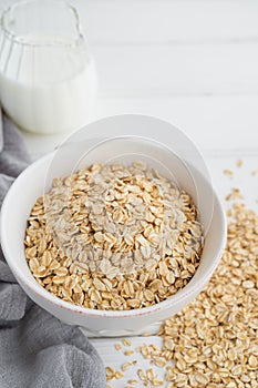 Raw dry oatmeal flakes in a bowl with milk on a white wooden background. Healthy food. Copy space