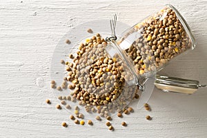 Raw, dry, uncooked brown lentil legumes in glass storage jar on white wood table background flat lay top view from above
