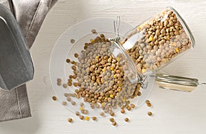 Raw, dry, uncooked brown lentil legumes in glass storage jar on white wood table background flat lay top view from above