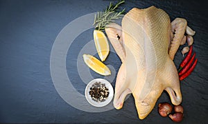 Raw duck with spices ready to cook on black background , fresh duck meat on plate for food , whole duck and lemon rosemary chili