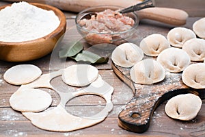 Raw dumplings on the cutting board and ingredients for their preparation: flour, egg, minced meat