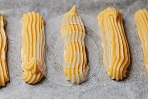 Raw eclairs choux pastry on the baking tray