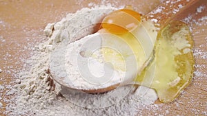 Raw egg falls into a pile of white flour in a wooden spoon.