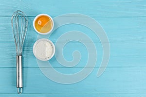 Raw egg, flour and whisk on blue wooden table, flat lay with space for text. Baking pie