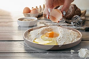 raw egg in hand is broken and poured into stylish bowl with flour on background of ingredients for baking at home. selective focus