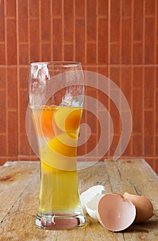 Raw Egg with Yellow Yolk in a glass and Broken Shell Halves