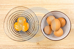 Raw eggs in ceramic bowl and egg yolks in glasses bowl