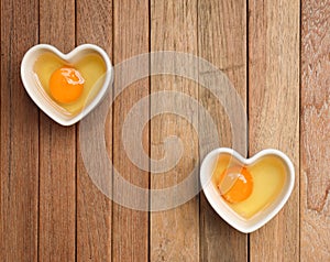 Raw eggs are in a heart shaped container for preparing cooking on a wooden  background