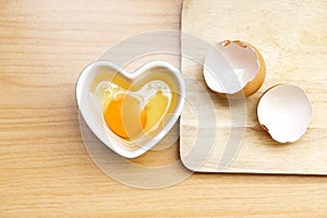 Raw eggs are in a heart shaped container for preparing cooking on a wooden  background