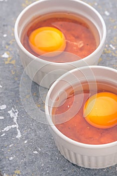 Raw eggs with tomatoes in the ramekins on the stone table vertical