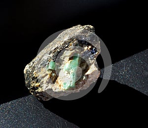 Raw emerald gemstone crystals inside feldspar rock with molybdenite, mica and apatite inclusions on black background